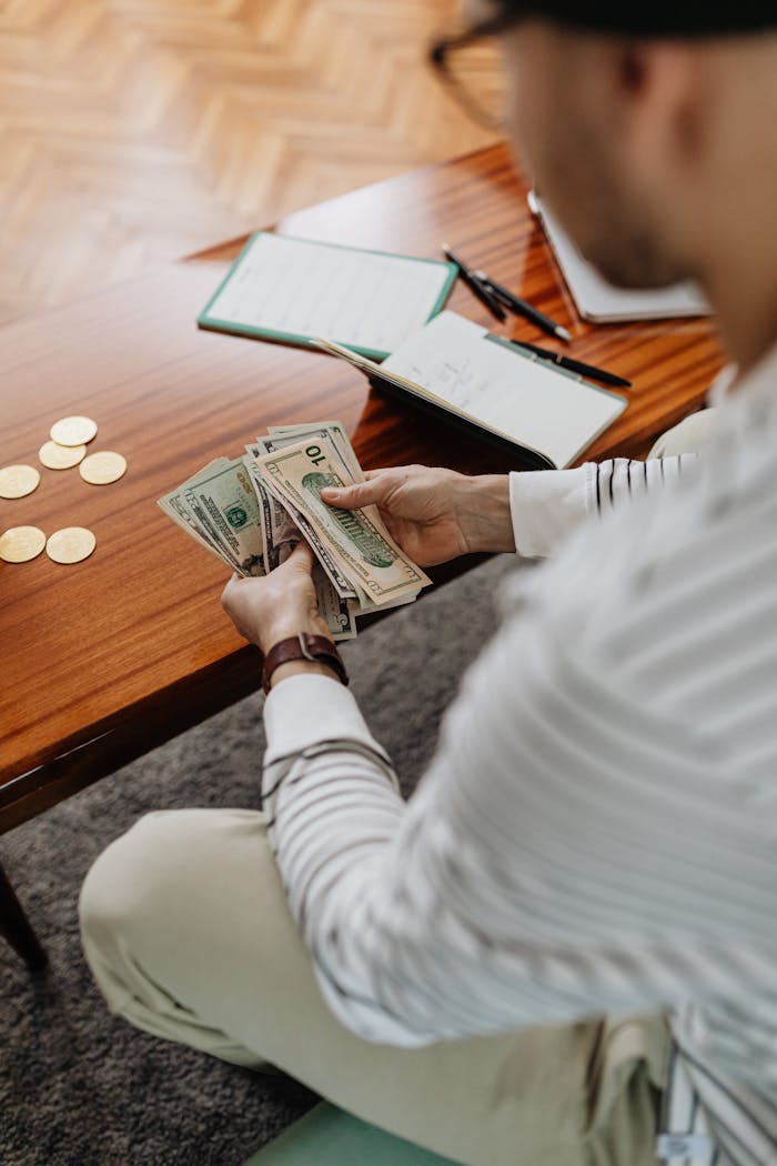 Individual counting dollar bills at a table with coins and a journal nearby.